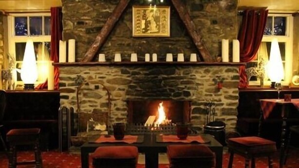A cozy room with a stone fireplace, a table with chairs, and a window with curtains. - The Luib Hotel (Crianlarich)