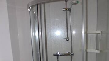 Une douche fermée par des parois en verre, dotée d’un pommeau de douche à main et d’un pommeau de douche fixe au plafond.