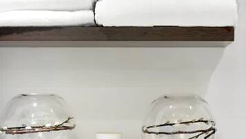 A shelf with folded white towels and two clear glass vases with branches.