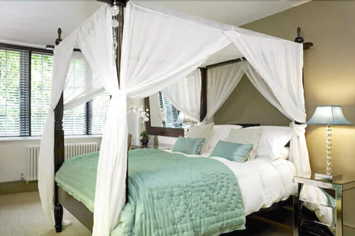 A four-poster canopy bed with a green quilt, white bedding, and a bedside table with a lamp.
