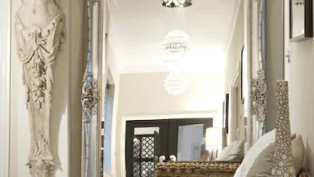 Una habitación con un espejo grande y ornamentado, un candelabro y un sofá de mimbre con cojines estampados.