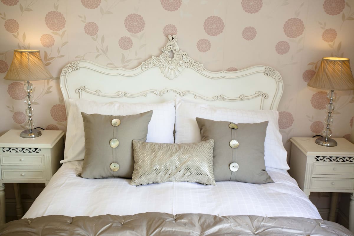 A neatly made bed with a decorative headboard, two bedside tables with lamps, and floral wallpaper.