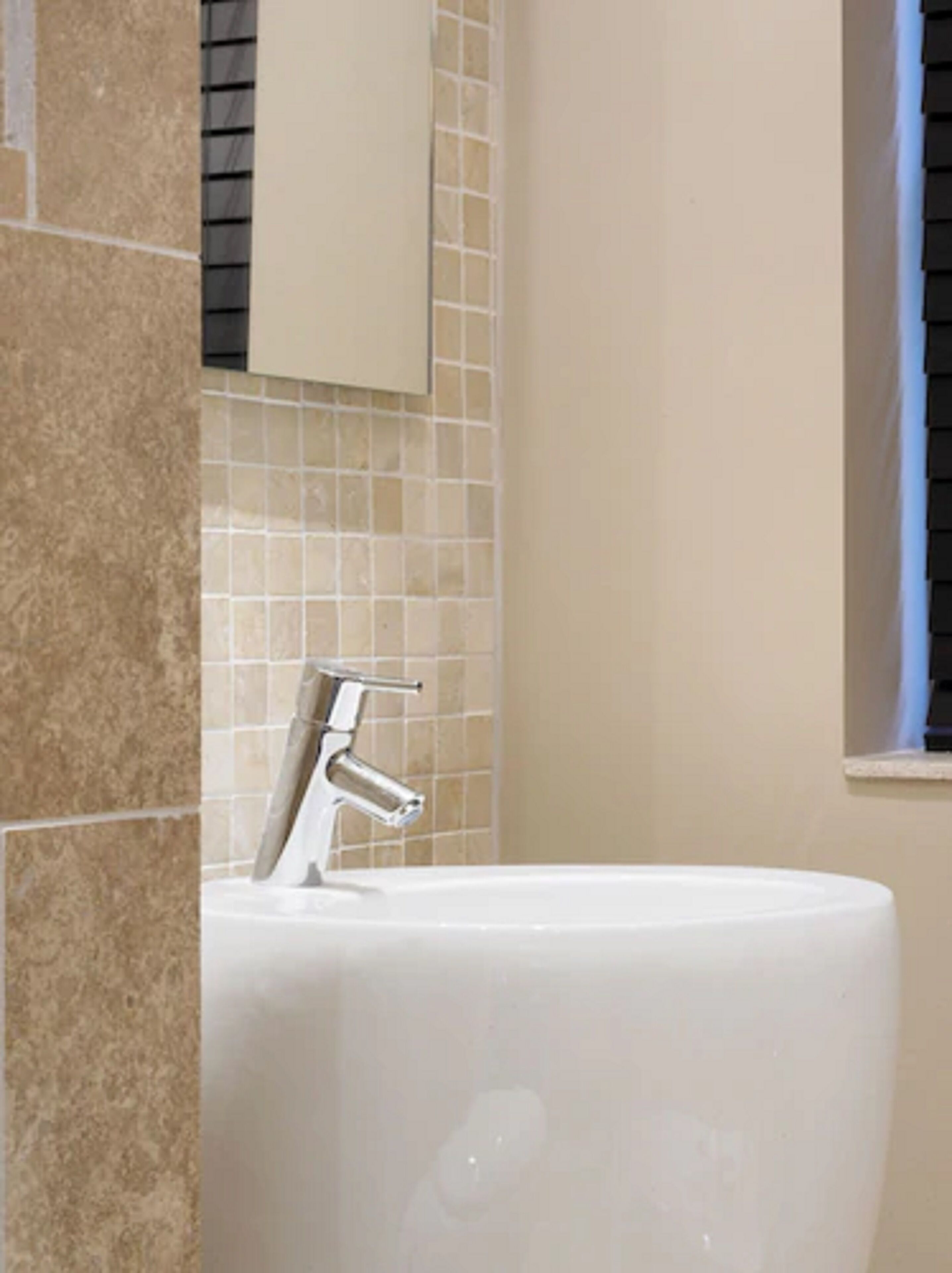 A bathroom with a white sink, a chrome faucet, and beige tiled walls.