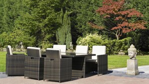 Un patio con mobiliario de mimbre, una estatua de Buda y abundante vegetación.