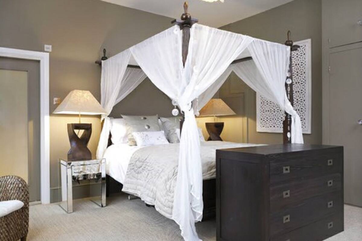 A bedroom with a four-poster bed, bedside lamps, a dresser, and a chair.