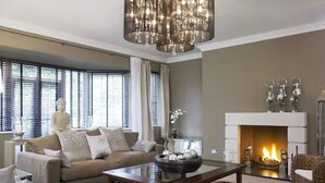 Una sala de estar con un sofá color beige, una mesa de centro de vidrio, una chimenea y una araña.