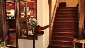 A grand staircase with a wooden finish, leading to an upper floor. A glass door with a view of a room with red walls and a desk is visible. A table with a vase of flowers is placed near the door. - Hotel Denkmal 13 – Rostock (Rostock)