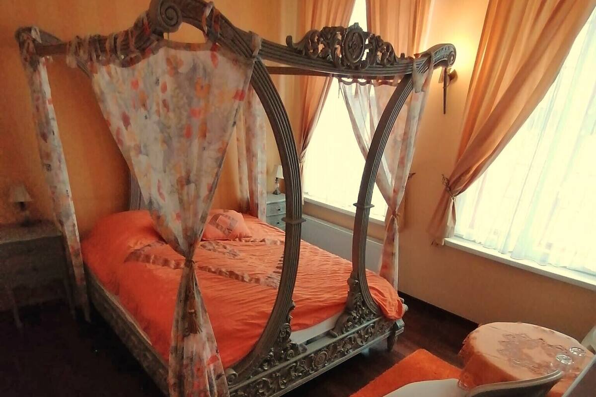 Ein Bett mit Baldachin, ein kleiner Schreibtisch mit Stuhl und ein Fenster mit Vorhängen.