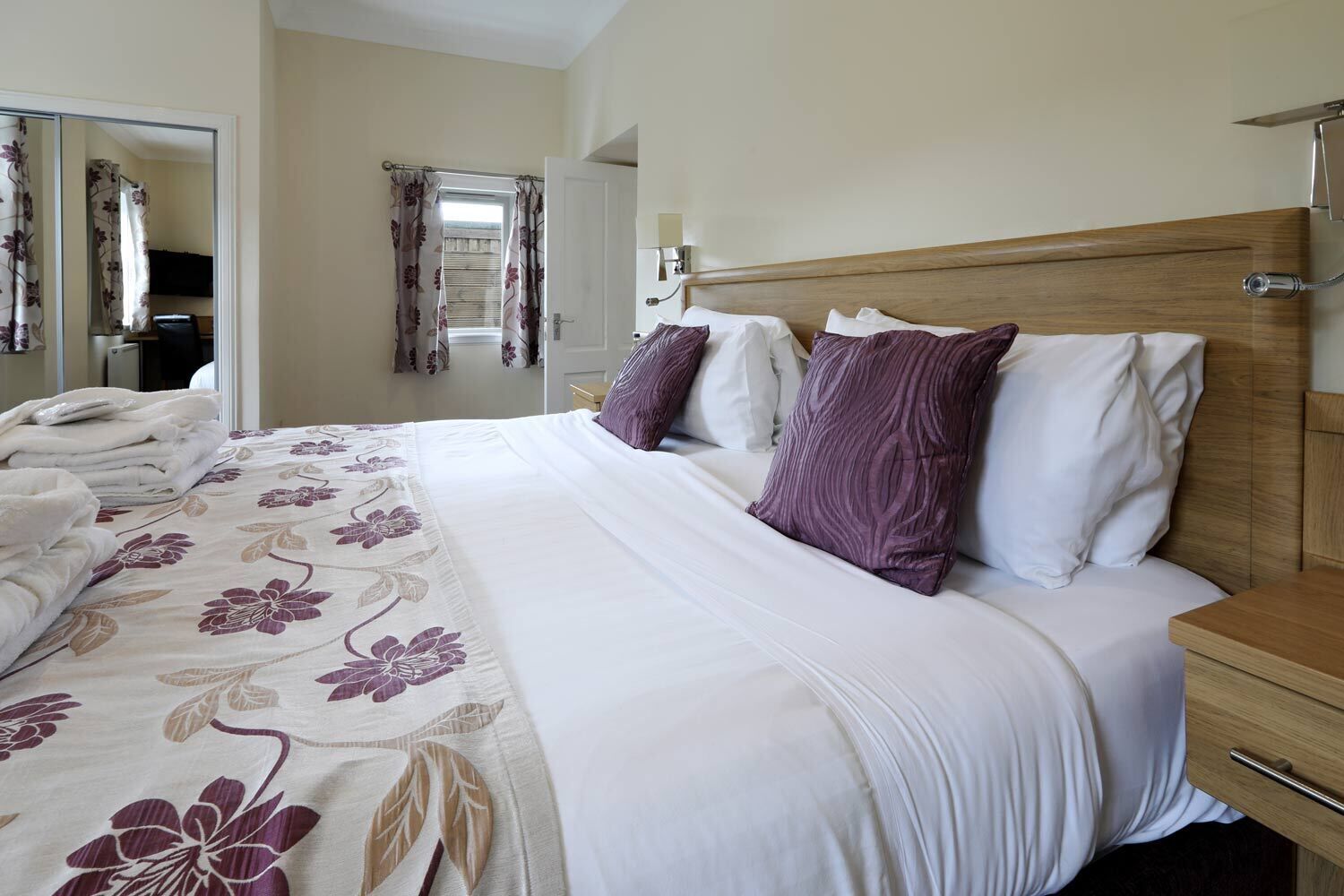 A neatly made bed with a floral bedspread, a wooden headboard, and a bedside table with a lamp.