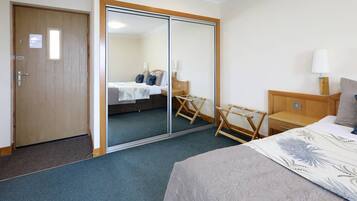 Una habitación de hotel con cama, una mesita de noche de madera, una silla, un espejo y una puerta.