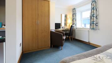 A hotel room with a wardrobe, a desk with a computer, a chair, a bed, and a window with curtains.