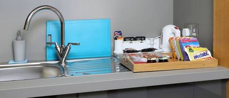 A modern kitchen with a stainless steel sink, a blue soap dispenser, a coffee maker, and a tray with snacks.