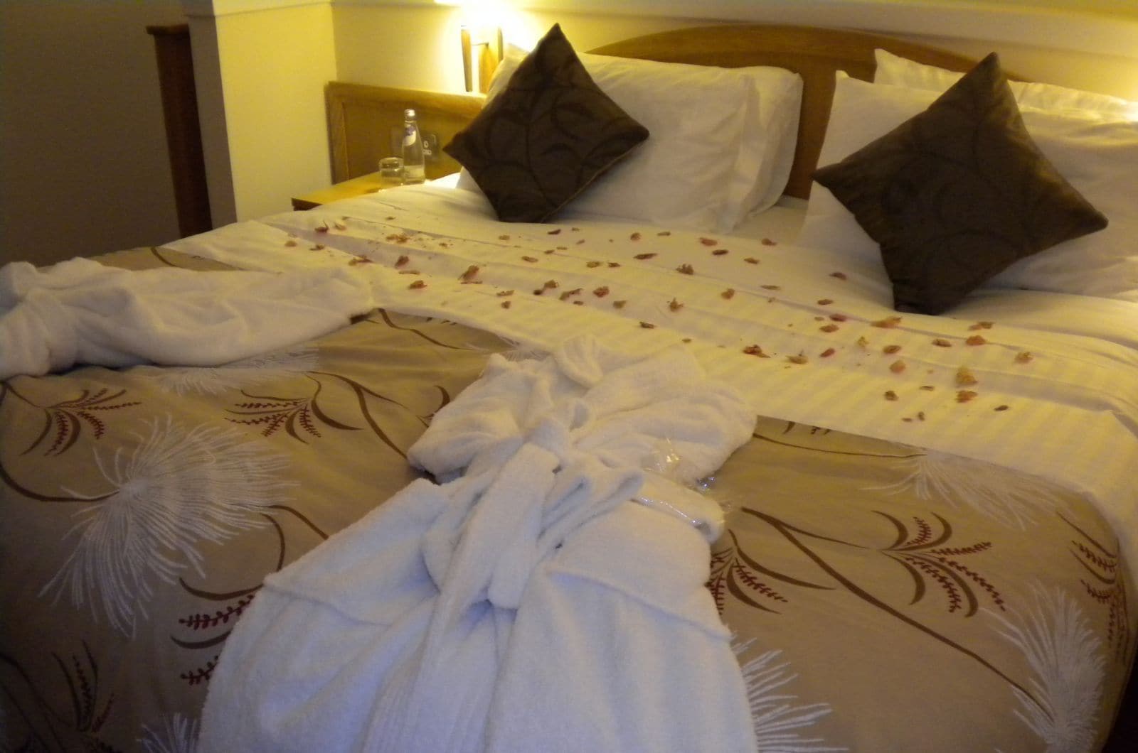 A neatly made bed with a floral bedspread, two pillows, and a bottle of water on a bedside table.