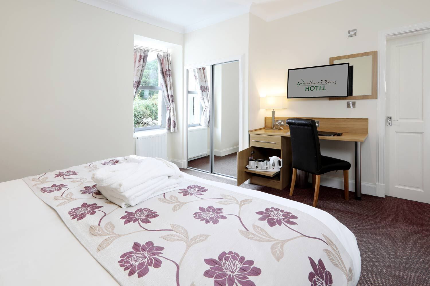 Een hotelkamer met een bed, bureau, stoel, televisie en een raam met gordijnen.