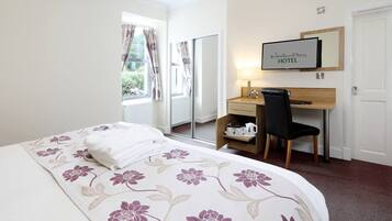 Een hotelkamer met een bed, bureau, stoel, televisie en een raam met gordijnen.