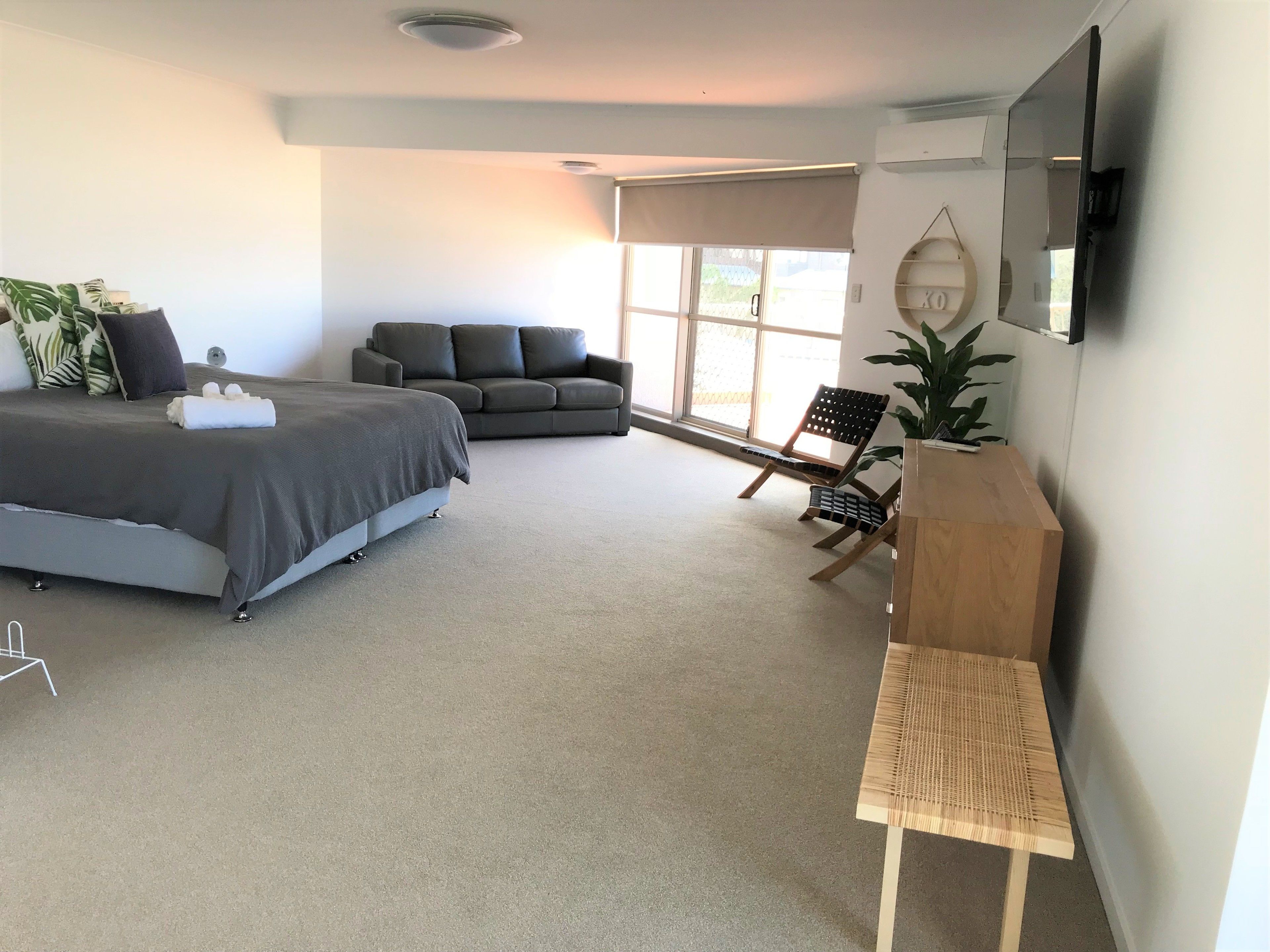 A modern bedroom with a bed, a sofa, a chair, and a TV.