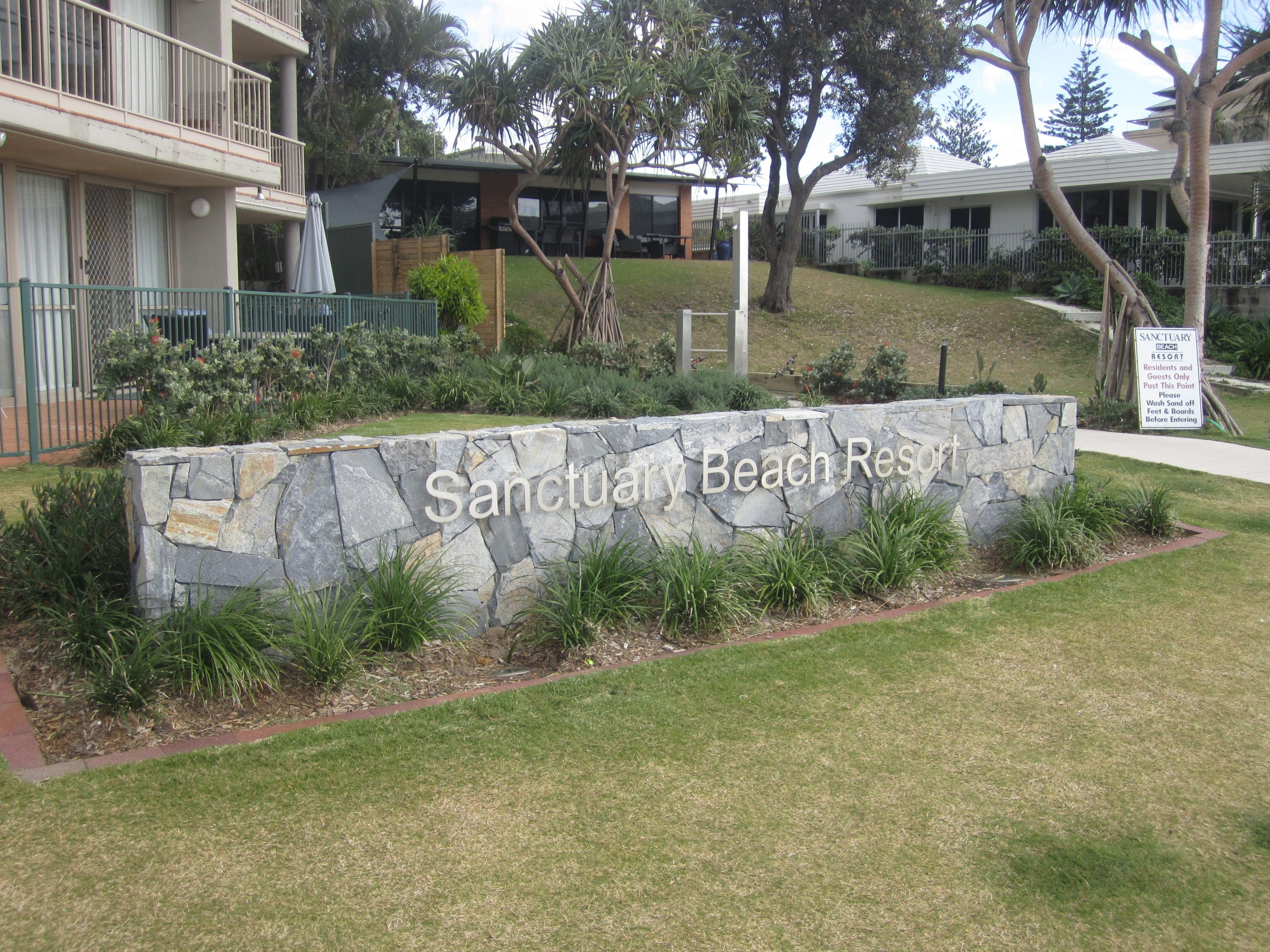 A stone wall with the text "Sanctuary Beach Resort" and a sign indicating a wash-off area for residents and guests.