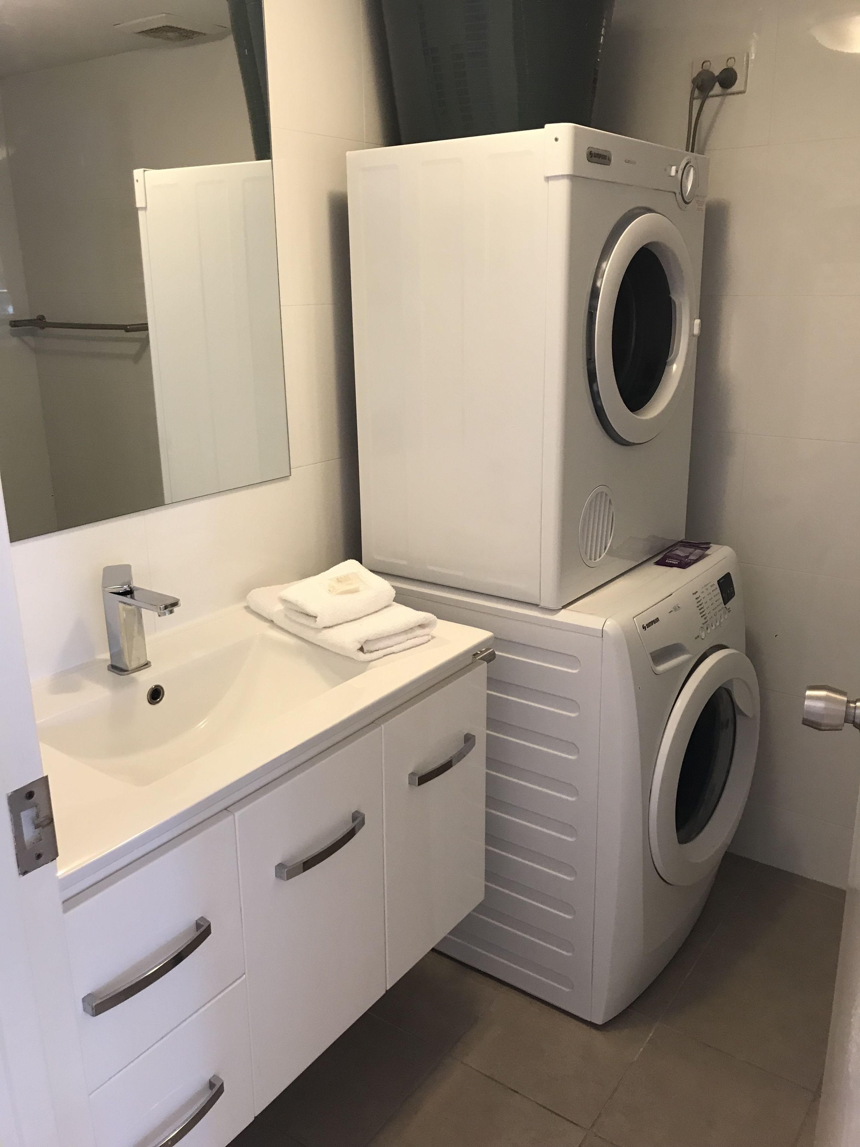A modern bathroom with a white sink, mirror, and stacked washer and dryer.