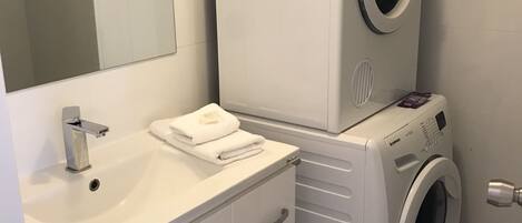 Un baño moderno con lavamanos blanco, espejo y lavadora y secadora apiladas.
