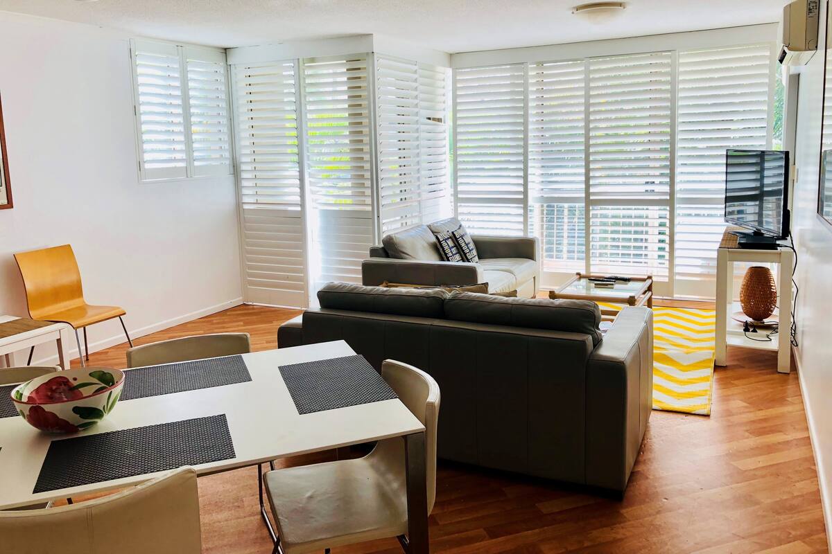 A modern living room with a sofa, a dining table with chairs, and a TV on a stand.