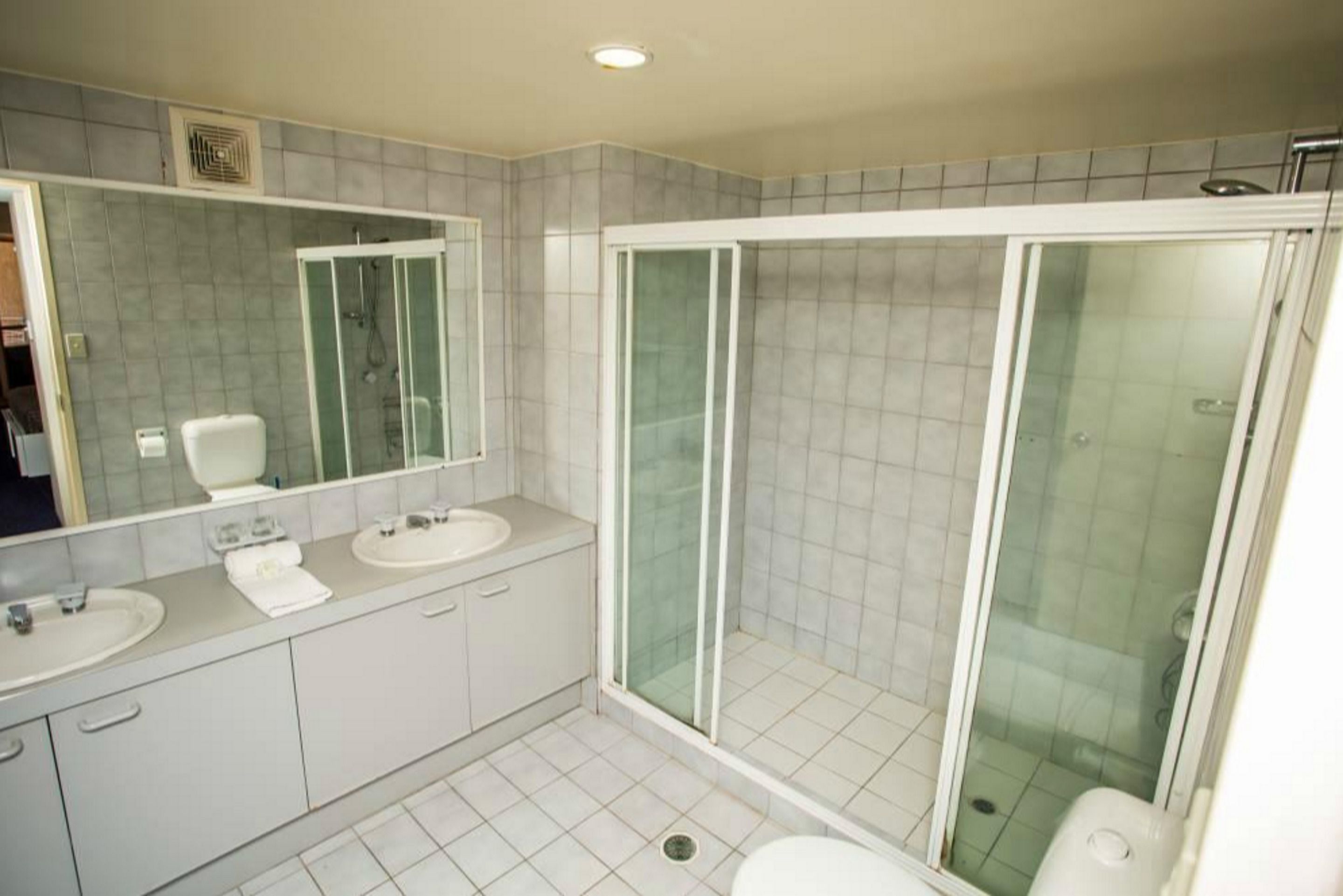 Un baño moderno con dos lavamanos, un espejo grande y una zona de ducha con mampara de vidrio.