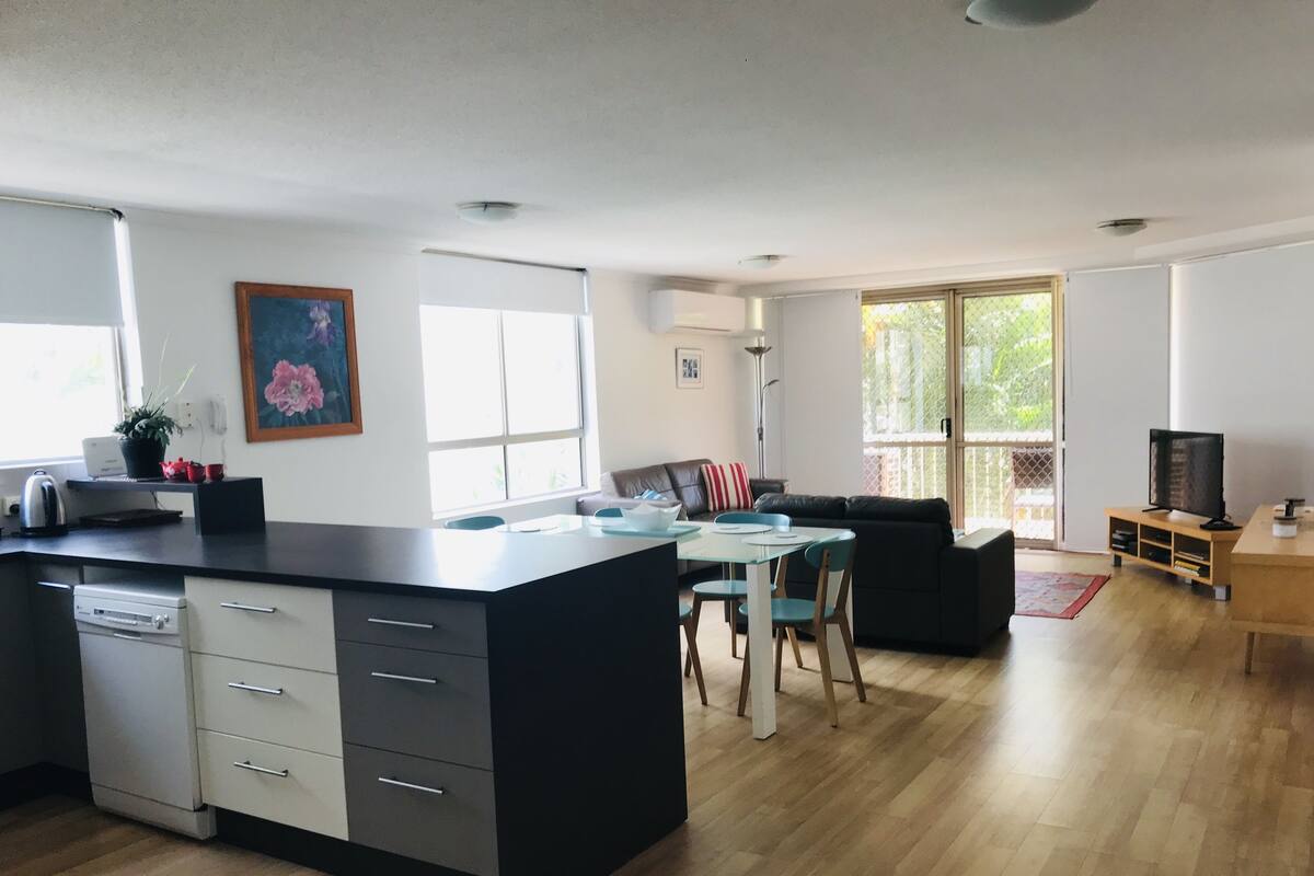 A modern kitchen with a central island, a dining area with a table and chairs, a sofa, and a television on a wooden stand.