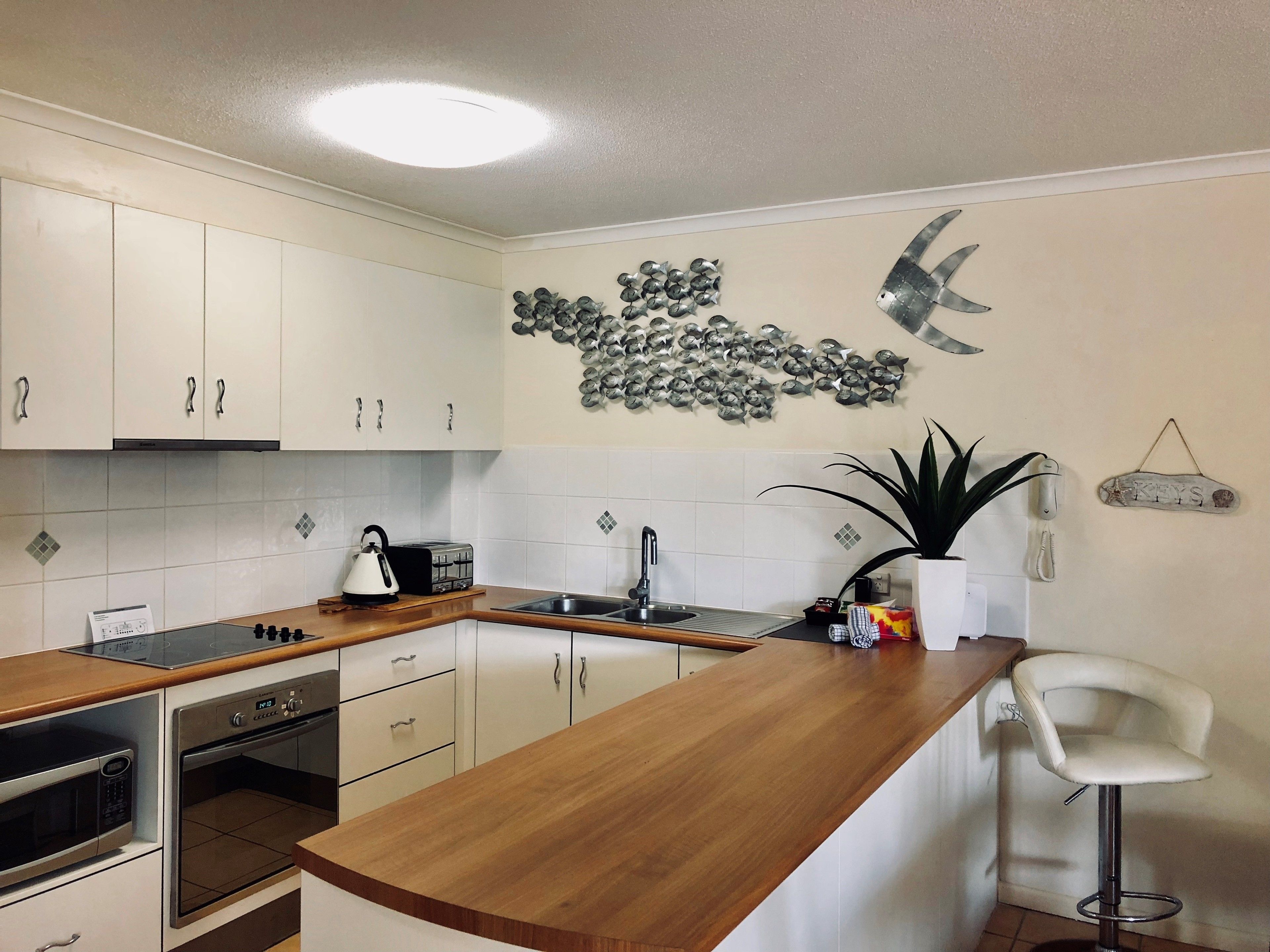 A modern kitchen with white cabinets, a wooden countertop, a built-in oven, a microwave, a toaster, a sink, and a decorative fish wall art piece.