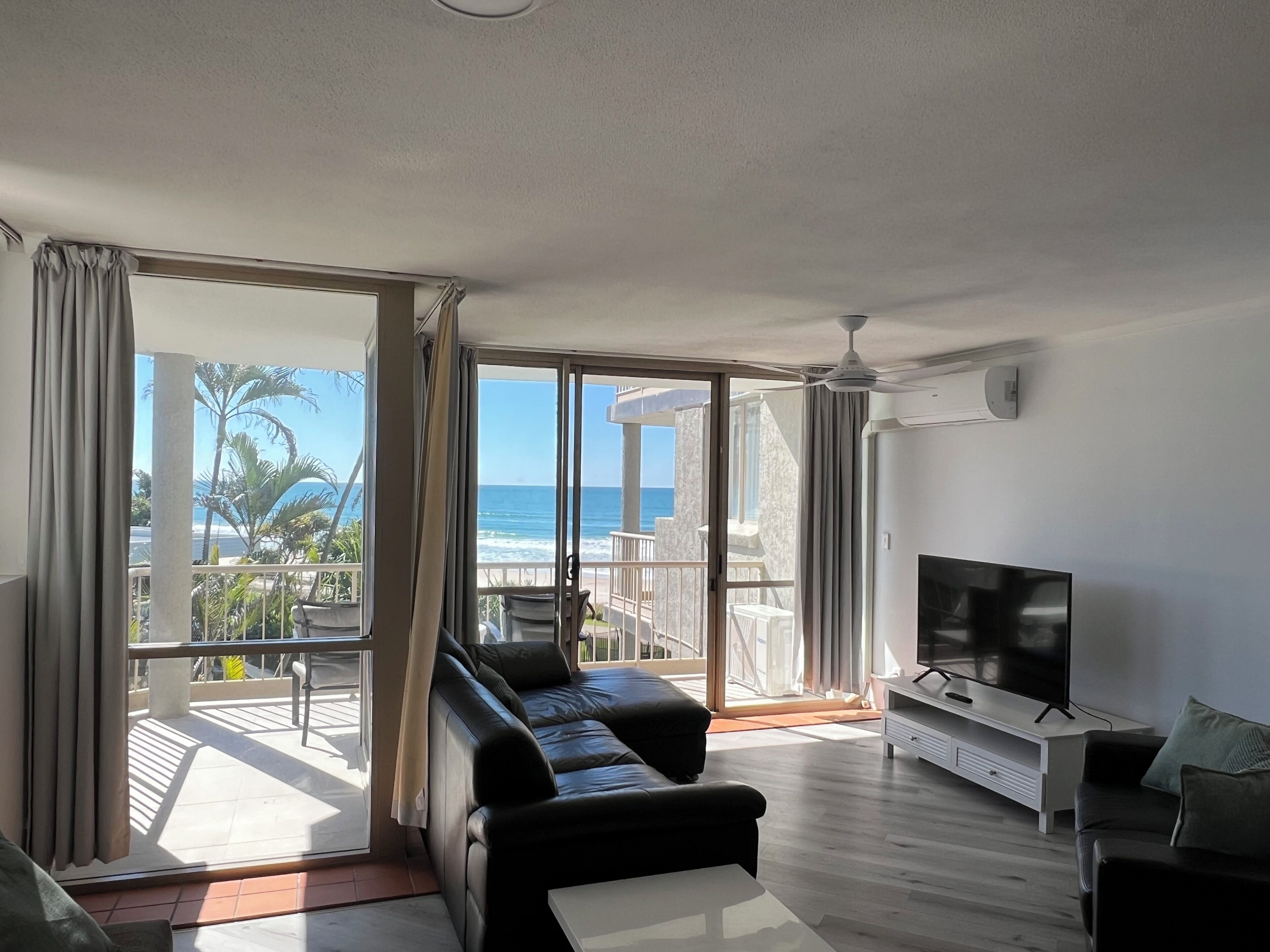 A modern living room with a large sliding glass door leading to a balcony with a view of the ocean.