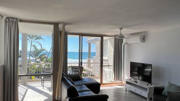A modern living room with a large sliding glass door leading to a balcony with a view of the ocean.