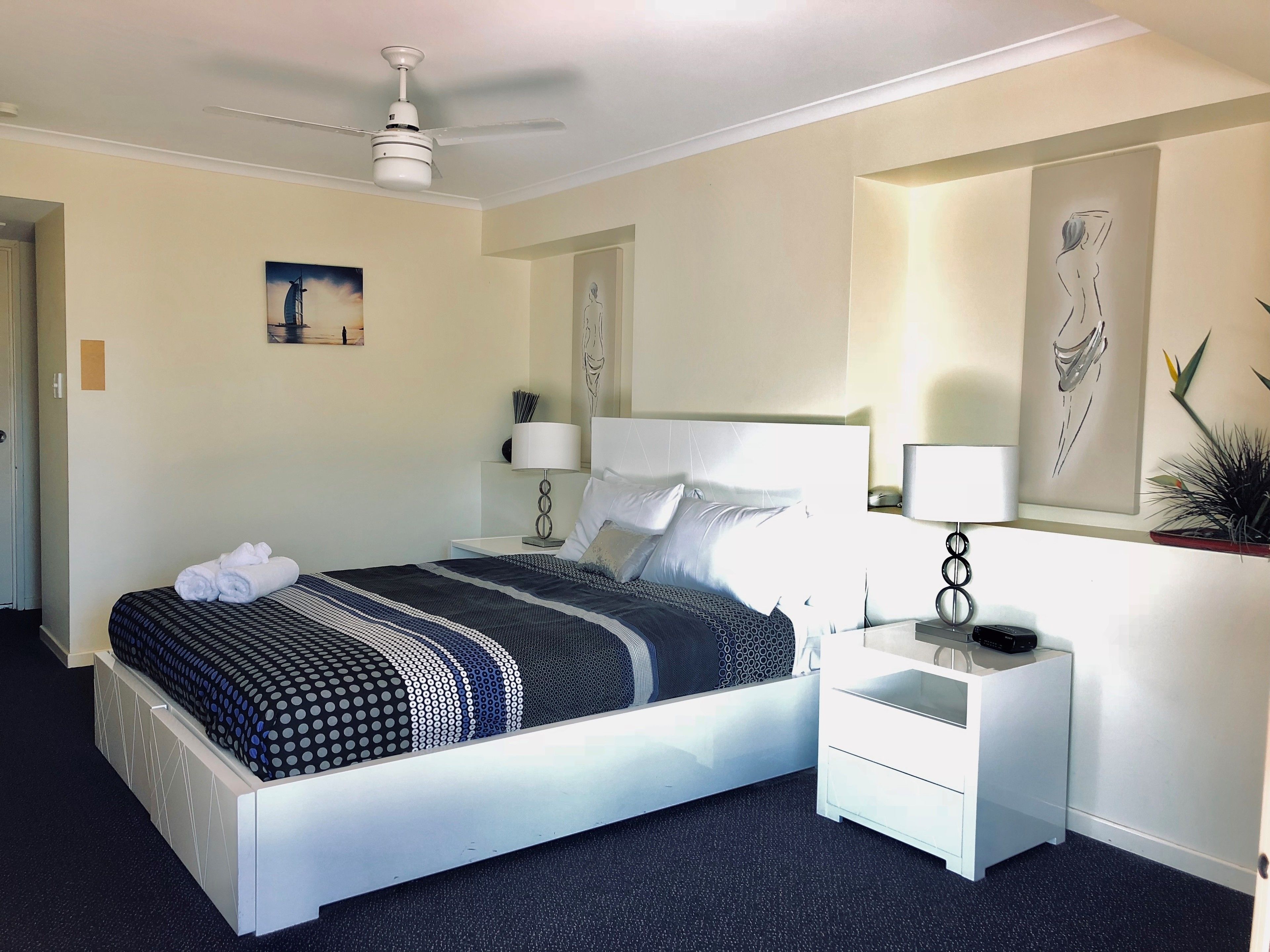 A modern hotel room with a large bed, a bedside table with a lamp, and artwork on the walls.