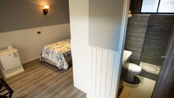A bedroom with a bed, a bedside table, and a nightstand. There is a window with a view of the outside.