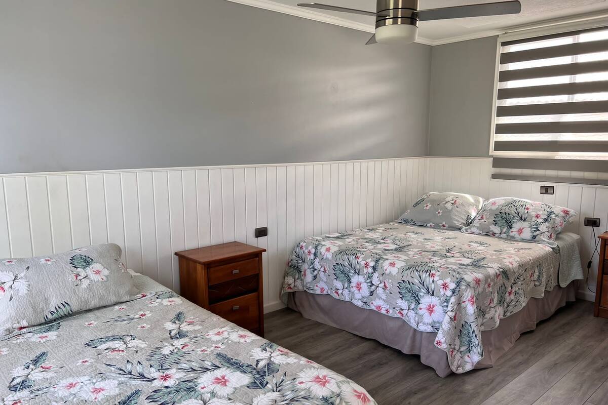 A bedroom with two beds, a wooden nightstand, a ceiling fan, and a window with blinds.