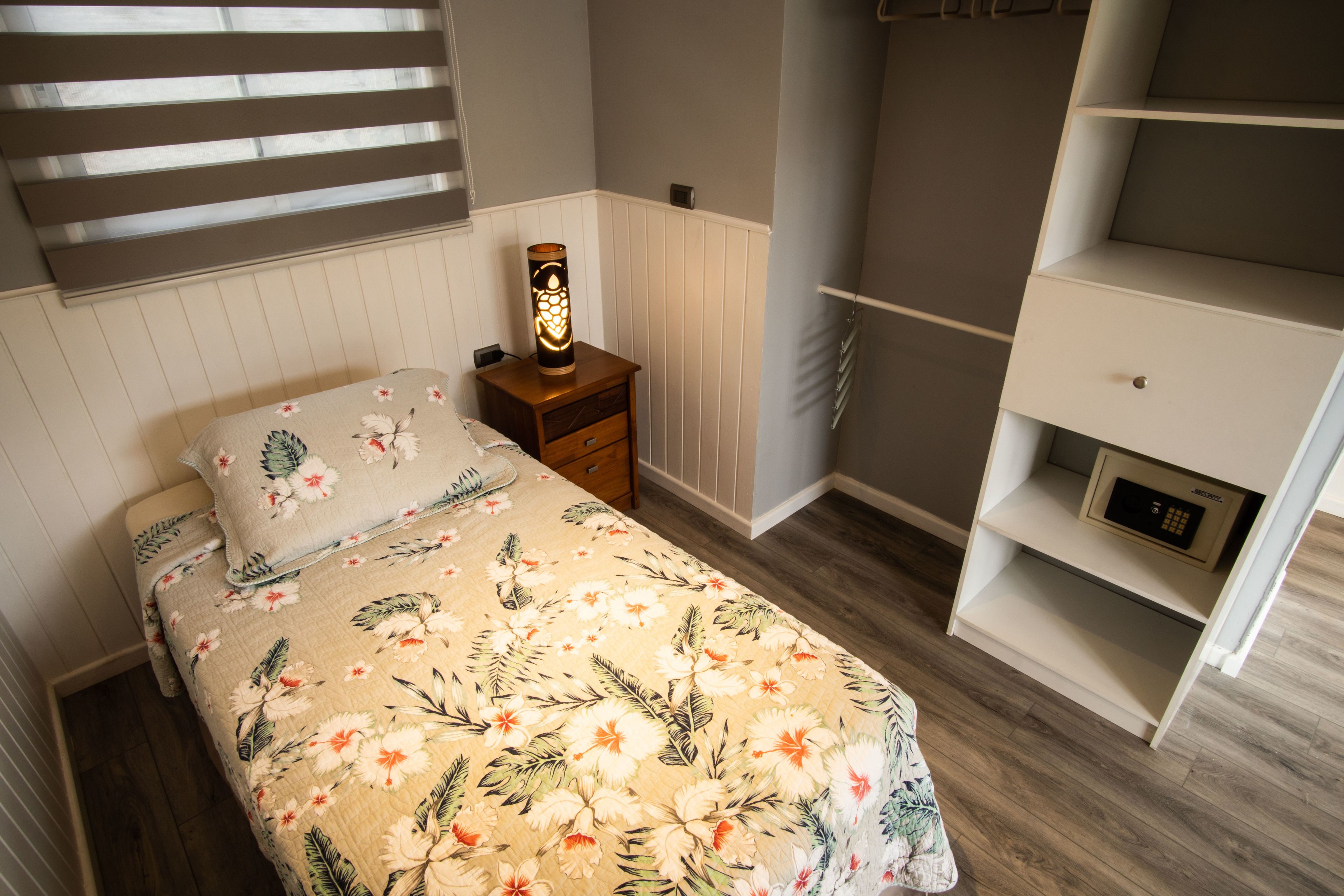 A bedroom with a floral bedspread, a bedside table with a lamp, a wardrobe, and a radiator.