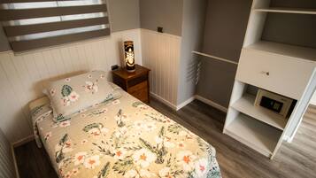 A bedroom with a floral bedspread, a bedside table with a lamp, a wardrobe, and a radiator.