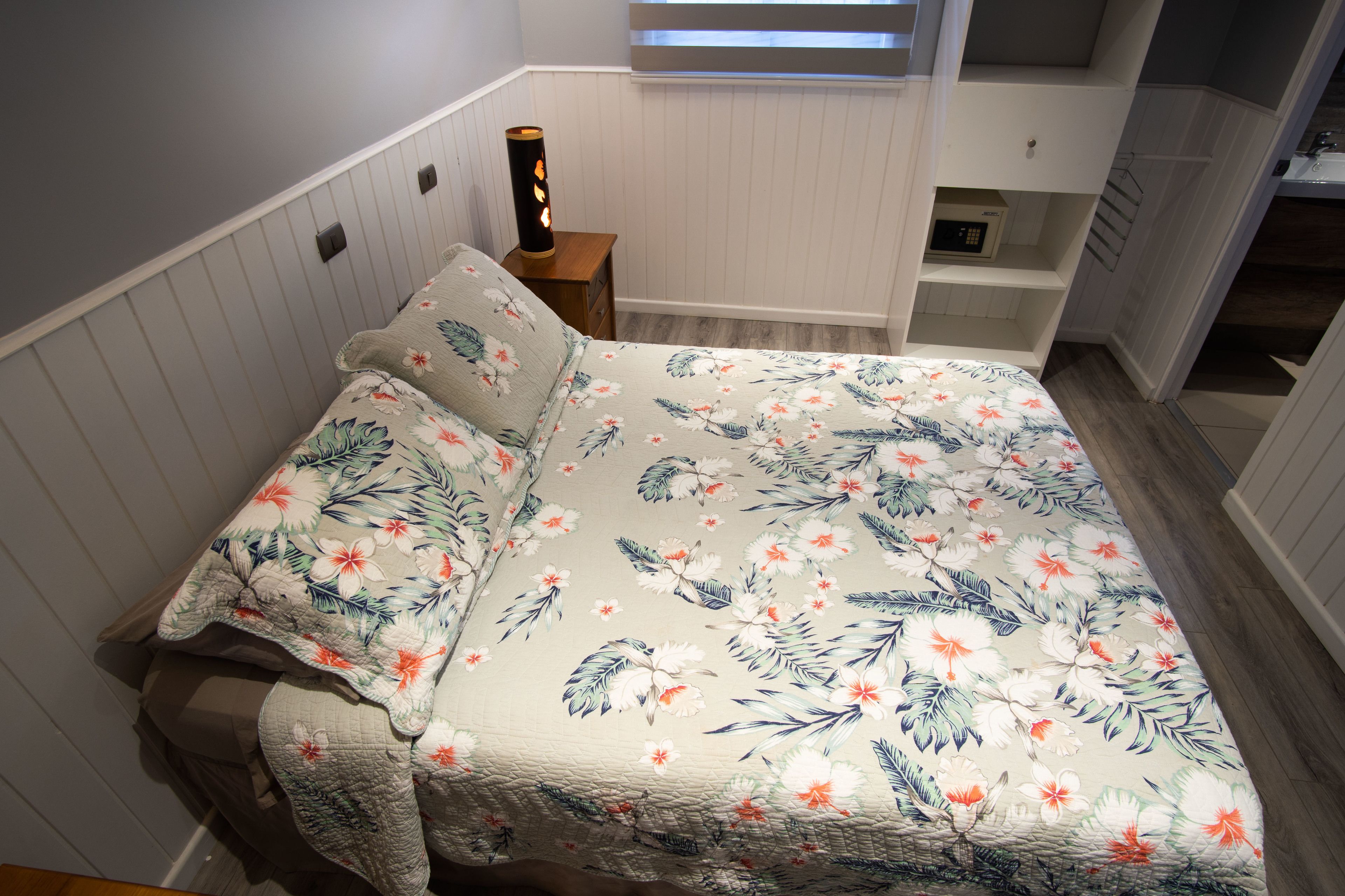 Une chambre à coucher avec une couvre-lit à motifs floraux, une table de chevet avec une lampe et une vue sur la salle de bain.