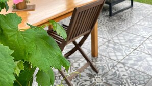 Un porche cubierto con una mesa y sillas de madera, un sofá y un suelo estampado.
