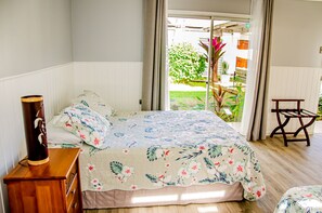 Un dormitorio con una cama, una mesita de noche de madera, una silla y vista al jardín a través de la ventana.