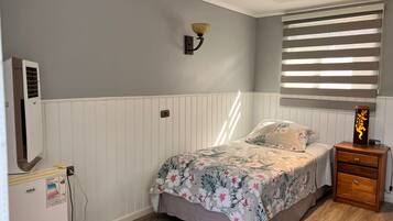 Een slaapkamer met een bed, een nachtkastje, een wandlamp, een raam met zonwering, en een luchtverfrisser.