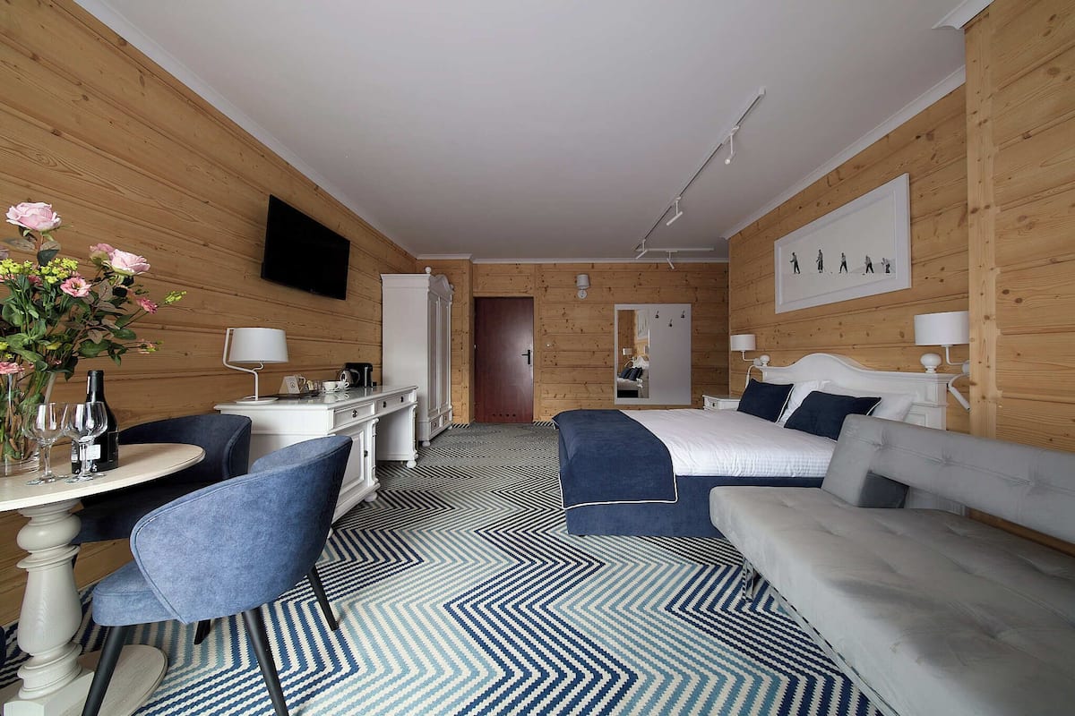 A hotel room with a wooden interior, a bed, a desk, a chair, and a TV on the wall.