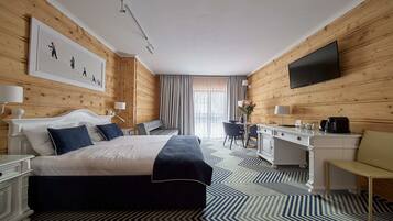 Quarto de hotel com cama, escrivaninha, cadeira e televisão na parede.
