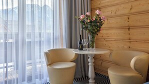 Una habitación con pared de madera, una mesa con sillas, un jarrón con flores y vistas a montañas a través de cortinas traslúcidas.