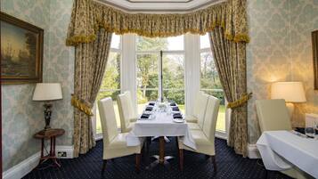 A dining room with a table set for four, two chairs on each side, a window with curtains, and a lamp on each side of the table.