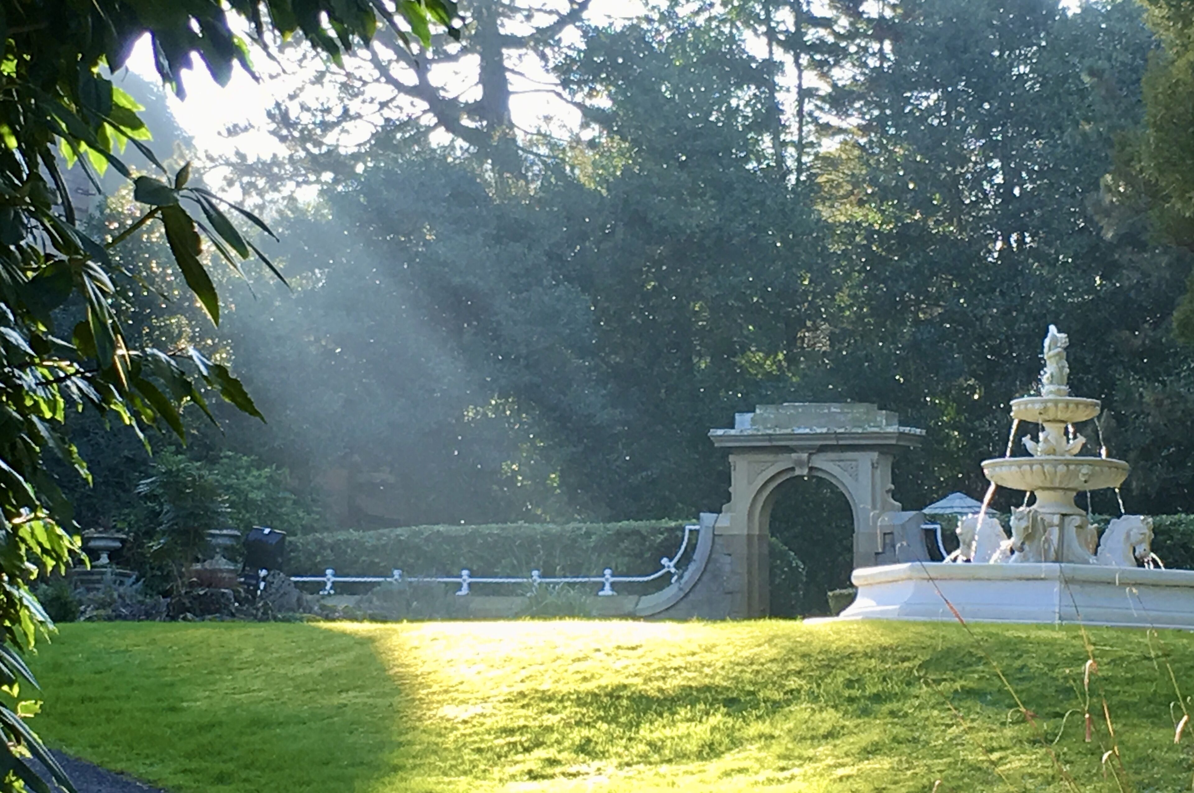 A park with a fountain, a stone archway, and a well-maintained lawn.