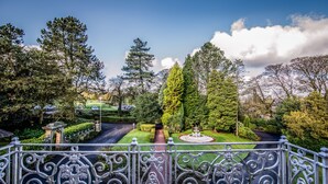 Un jardín con una fuente, setos perfectamente recortados y árboles altos.