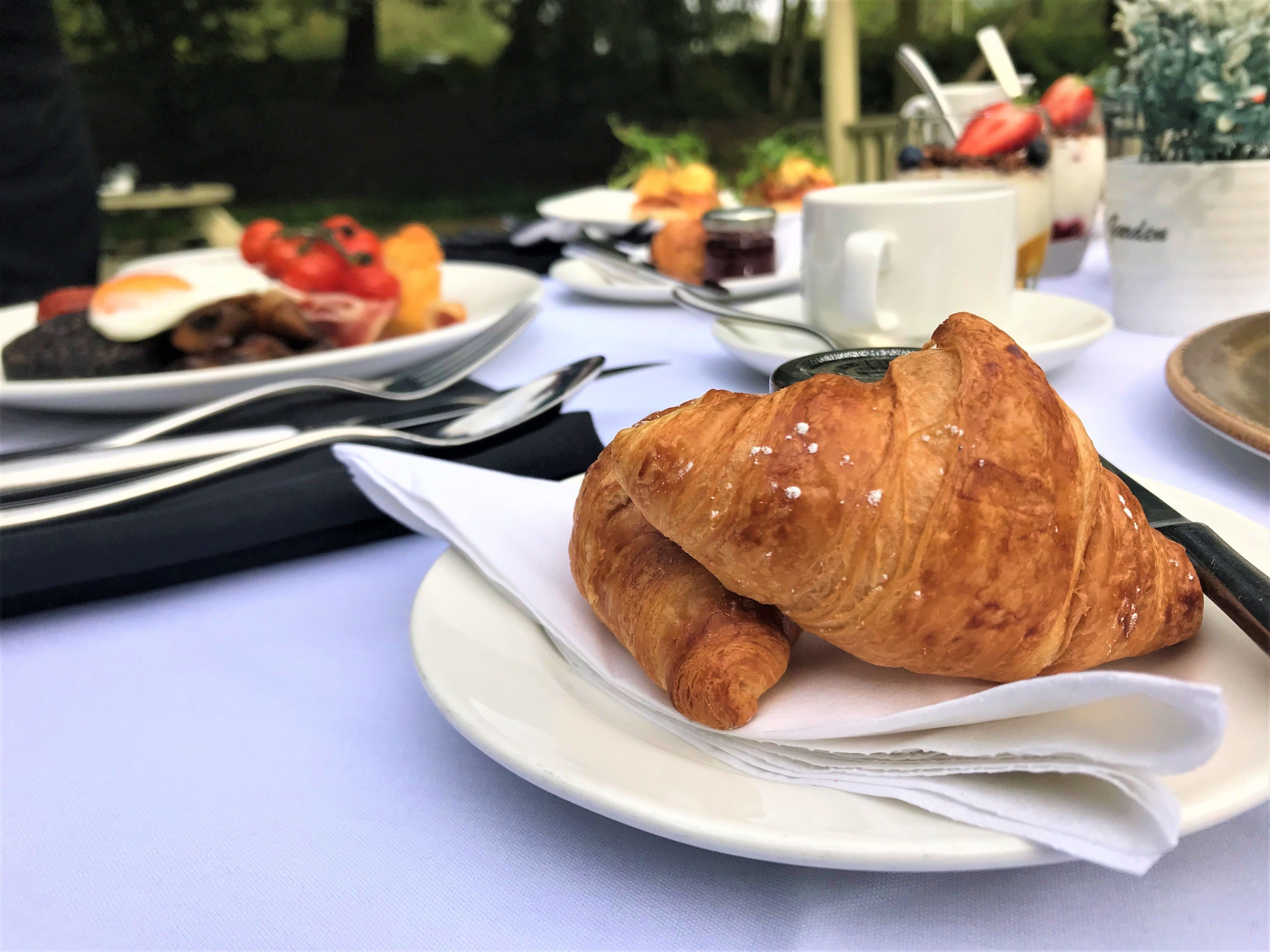 A table set with plates of food, including a croissant, and a cup.