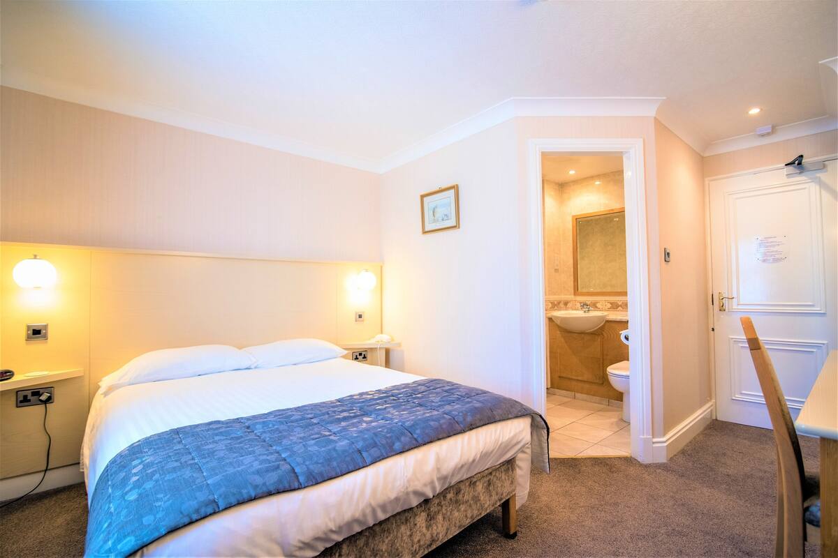 A hotel room with a bed, bedside lamps, a bathroom with a sink and toilet, and a wooden chair.