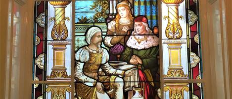 A stained glass window with the inscription "Othello's Story" and a depiction of a man and a woman in historical attire.