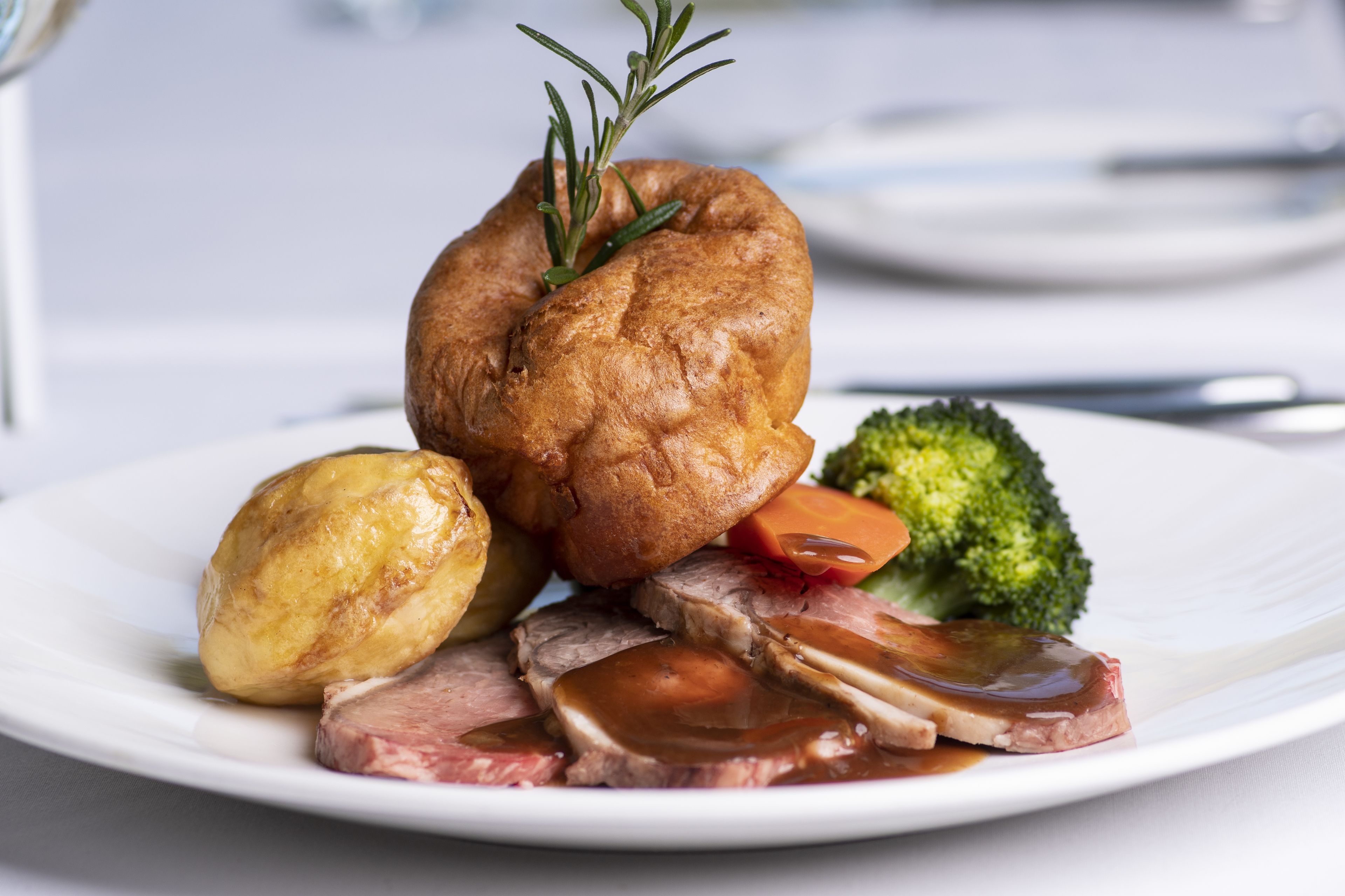 A plate with roast beef, Yorkshire pudding, a baked potato, and steamed vegetables.