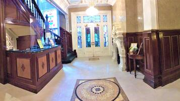 A grand hallway with a marble floor, a staircase, and a large wooden door with stained glass.