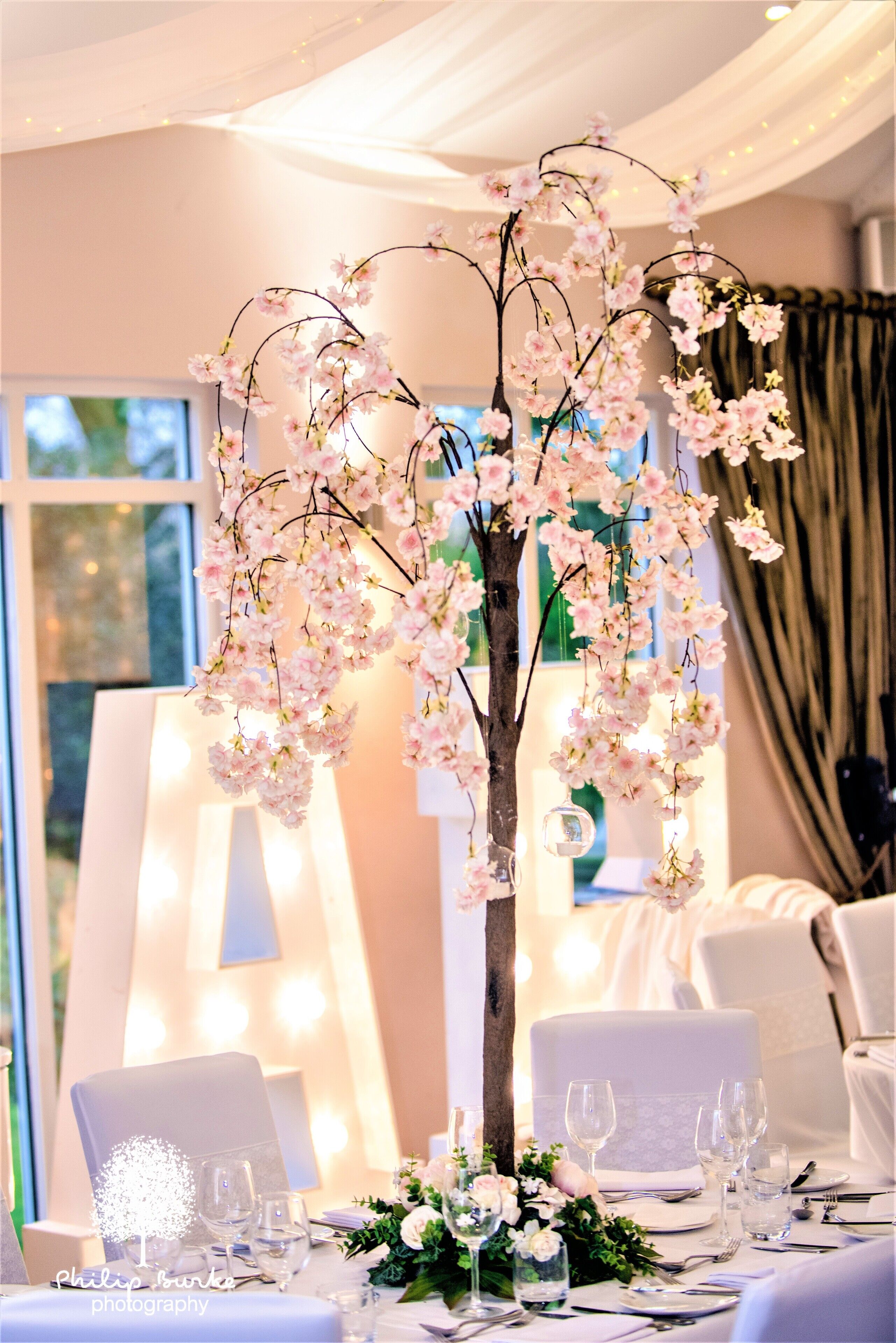 A table set for a formal event with a floral centerpiece, white tablecloths, and clear glassware.